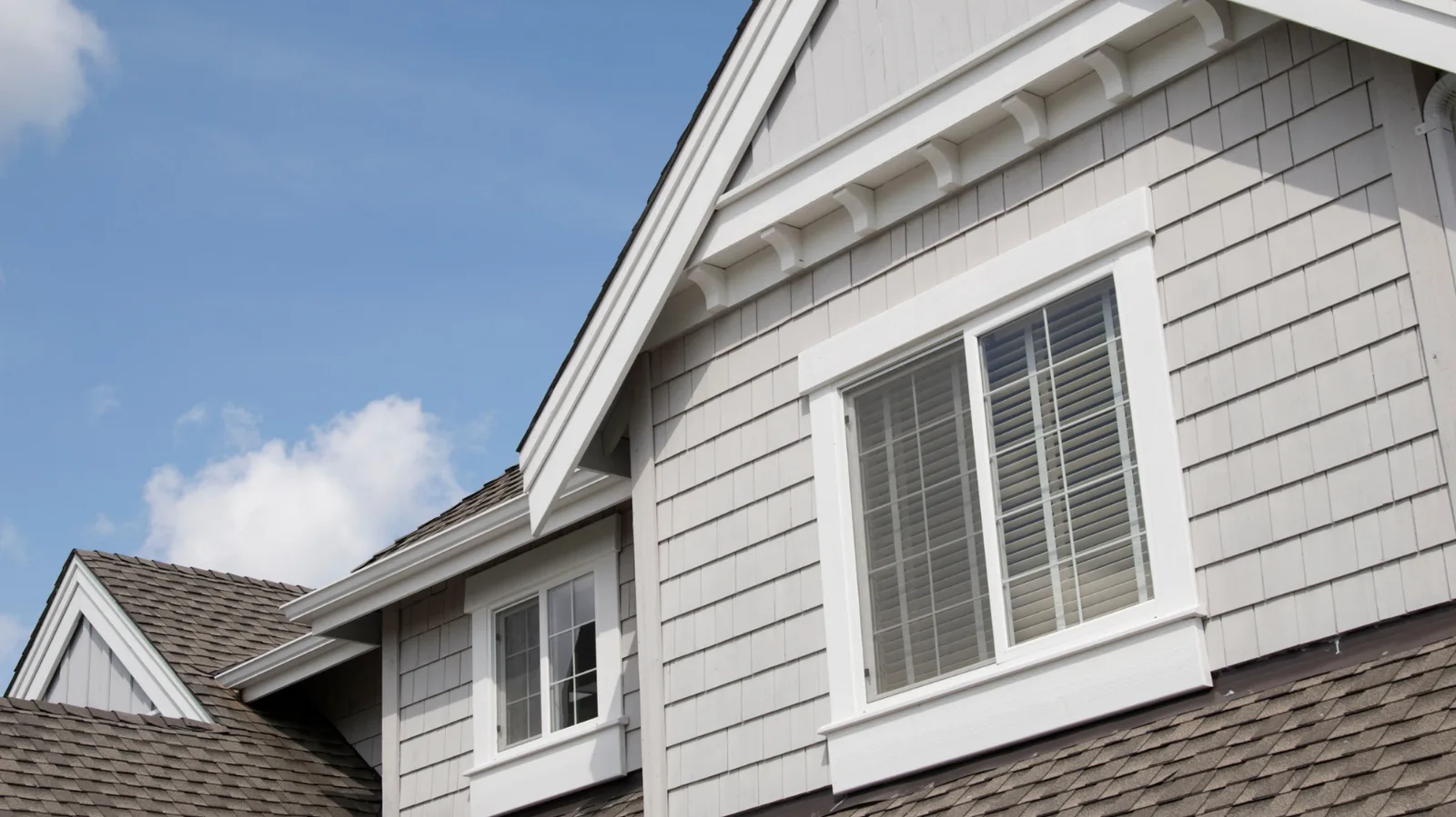 Brown asphalt shingle rooflines beside white-trimmed gables