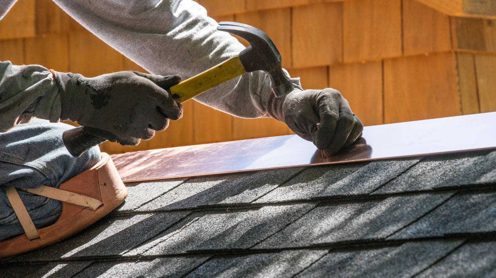 Gloved hands fastening copper flashing beside asphalt shingles